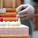 A decorator's hands carefully piping frosting onto a multi-layered cake.