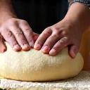 Hands of a baker kneading a large ball of dough on a floured surface.